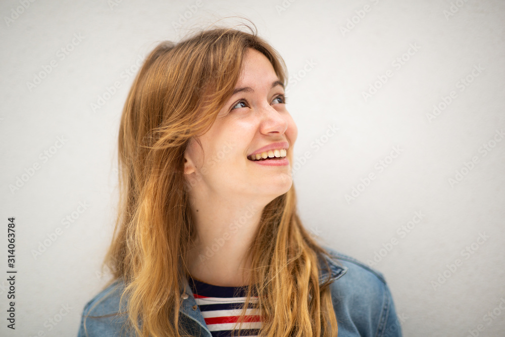 Close up young woman with long blond hair smiling and looking away by white background Close up young woman with long blond hair smiling and looking away by white background