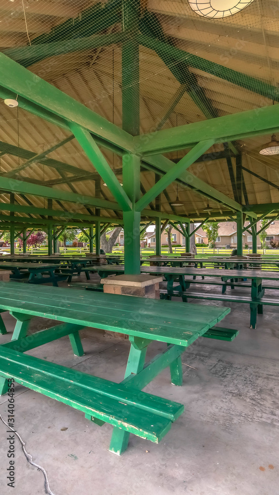 Vertical frame Interior of pavilion with green picnic tables and seats at a park on a sunny day