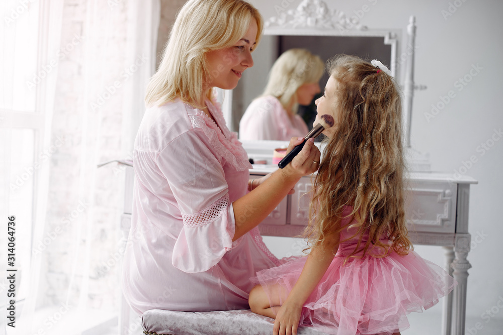 Family sitting infront a mirror. Mother in a pink pajamas. Little girl with cosmetics.