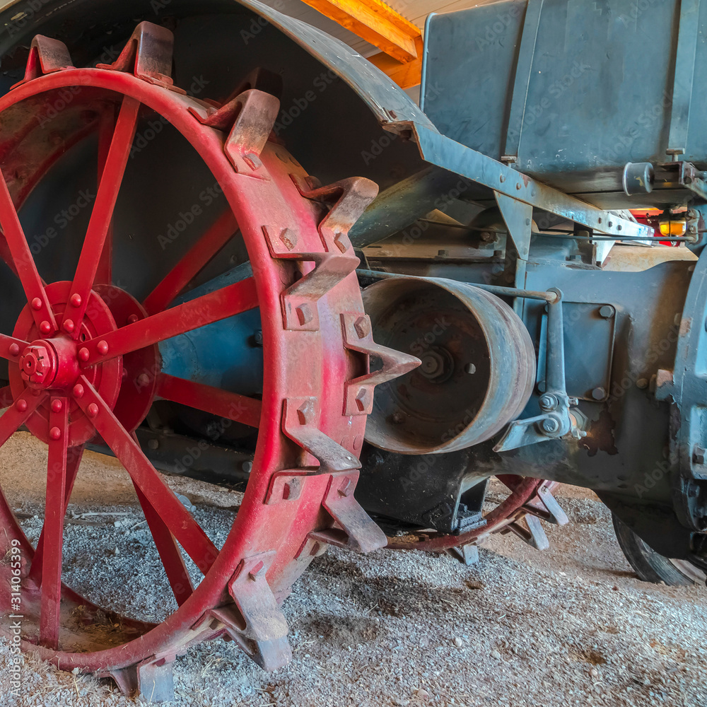 Square frame Red wheel rim of an and vintage tractor against stone wall of a farm barn