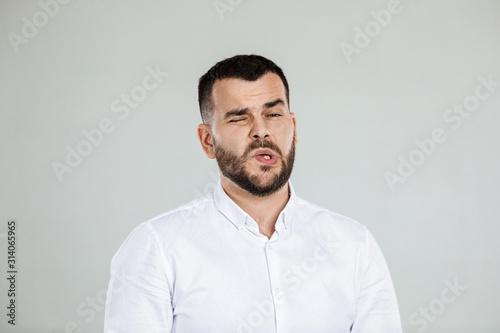 Portrait of young frowned handsome bearded man on gray background. facial expression. man grimaced