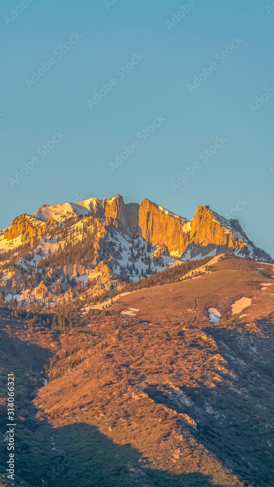 Vertical Striking mountain peak with rugged slopes against blue sky on a sunny day
