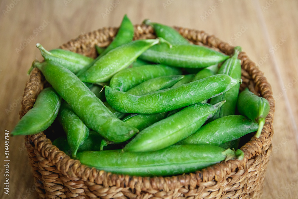 The crop of peas lies in a round wicker basket on a wooden background. Top view. Copy, empty space for text The crop of peas lies in a round wicker basket on a wooden background. Top view. Copy, empty space for text