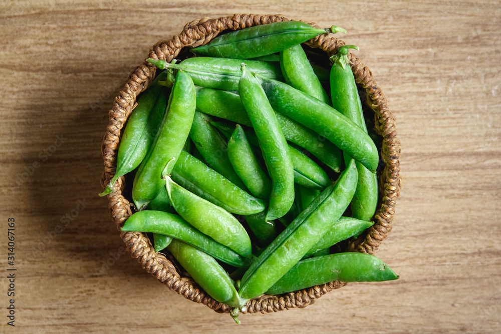The crop of peas lies in a round wicker basket on a wooden background. Top view. Copy, empty space for text The crop of peas lies in a round wicker basket on a wooden background. Top view. Copy, empty space for text