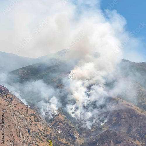 Square frame Mountain landscape with smoke from wild forest fire against clear blue sky © Jason