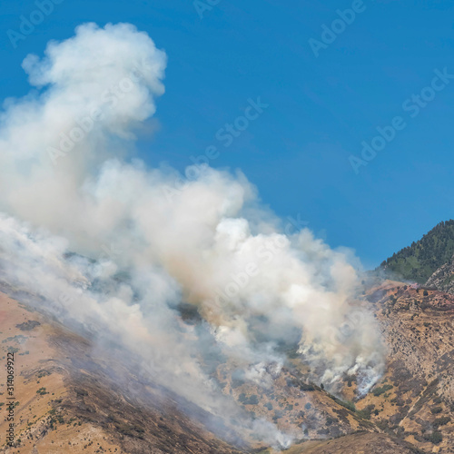 Square frame Thick puffs of smoke from fire in the mountain against clear blue sky background