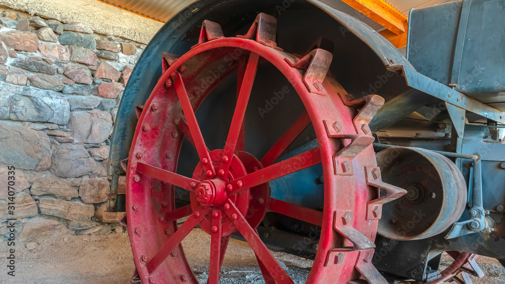 Pano Red wheel rim of an and vintage tractor against stone wall of a farm barn