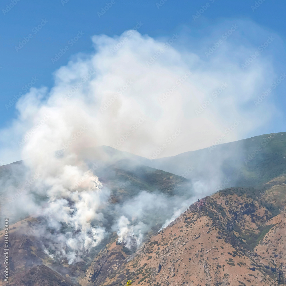 Square Mountain landscape with smoke from wild forest fire against clear blue sky