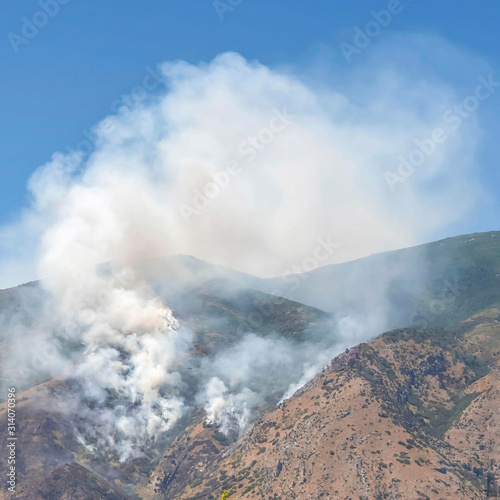 Square Mountain landscape with smoke from wild forest fire against clear blue sky