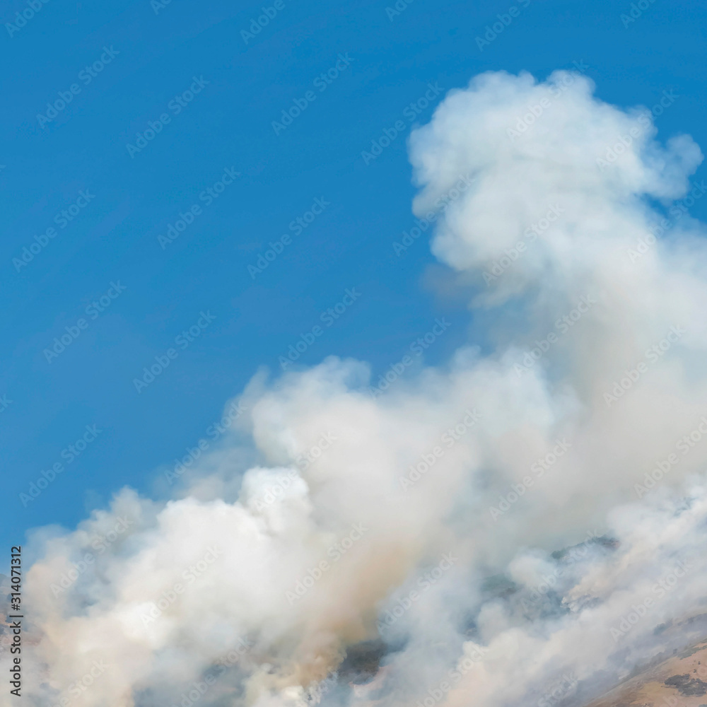 Square Thick puffs of smoke from fire in the mountain against clear blue sky background