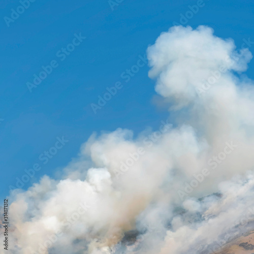 Square Thick puffs of smoke from fire in the mountain against clear blue sky background