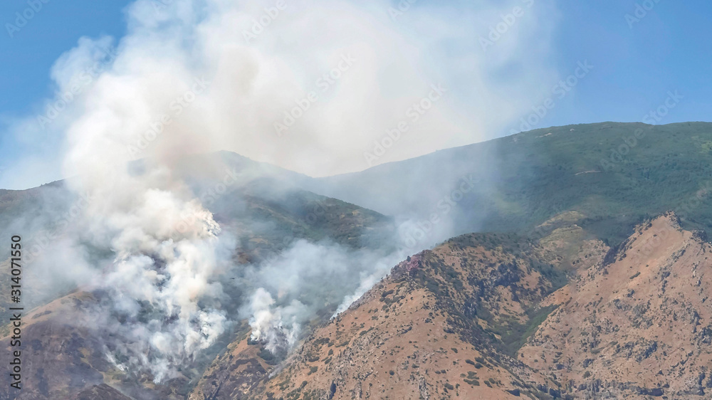 Pano frame Mountain landscape with smoke from wild forest fire against clear blue sky