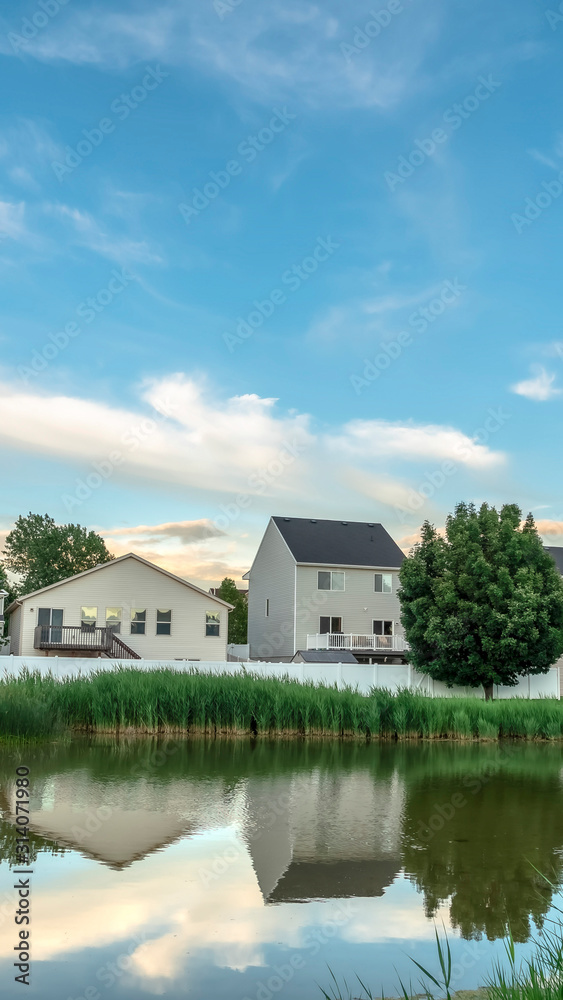 Vertical Scenic suburban landscape with homes and cloudy sky reflected on a shiny pond Vertical Scenic suburban landscape with homes and cloudy sky reflected on a shiny pond