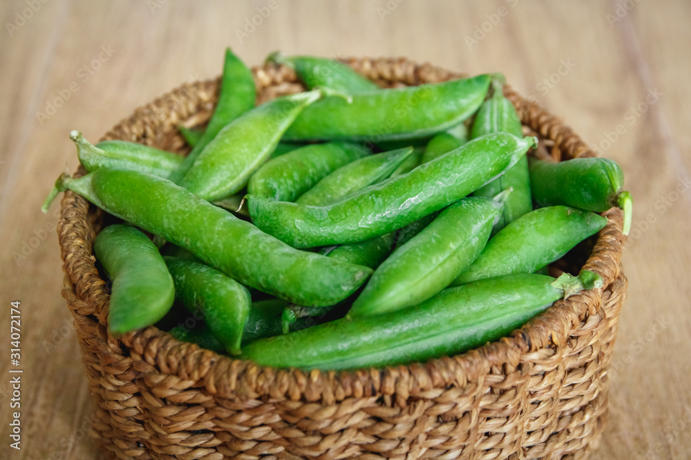 The crop of peas lies in a round wicker basket on a wooden background. Top view. Copy, empty space for text The crop of peas lies in a round wicker basket on a wooden background. Top view. Copy, empty space for text