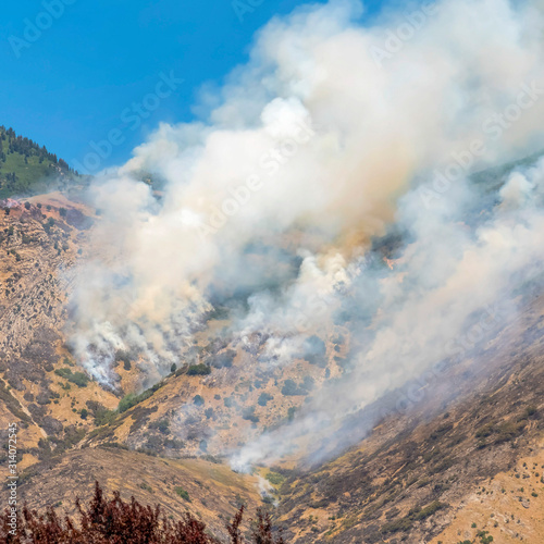 Square frame Aerial view of mountain top with vegetation and thick smoke against blue sky