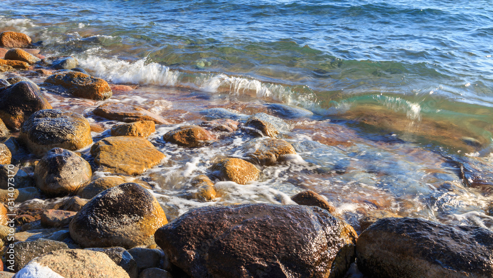 Stones on the sea beach. Pasture winter day. Clear water and sand. Kyrgyzstan, Issyk-Kul Lake