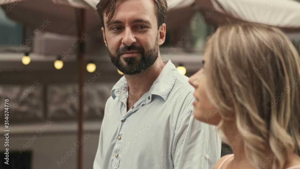 A positive happy couple man and woman are walking by street while talking to each other outdoors in summer 