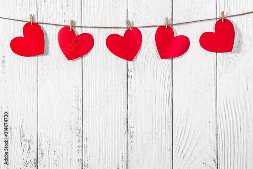 White painted wooden background with a garland of red hearts. Natural rope and clothespins. Concept of recognition of love, romantic relationships, Valentine's day in grunge style. Copy space