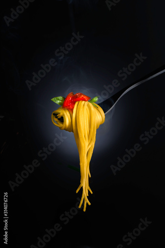 Spaghetti with tomato sauce and basil on a fork, with steam. Close-up shot, shallow focus.
