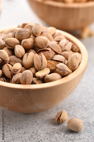 many pistachios in a wooden bowl on a light background. Vertical