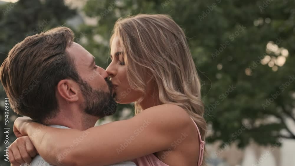 Cute young couple man and woman is hugging and kissing while walking at the city street in summer Cute young couple man and woman is hugging and kissing while walking at the city street in summer