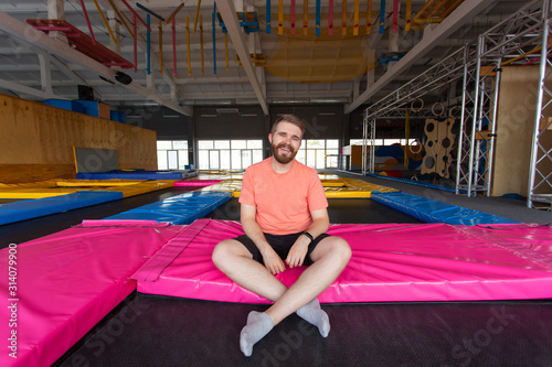 Fitness, fun, leisure and sport activity concept - Man sitting on a trampoline indoors