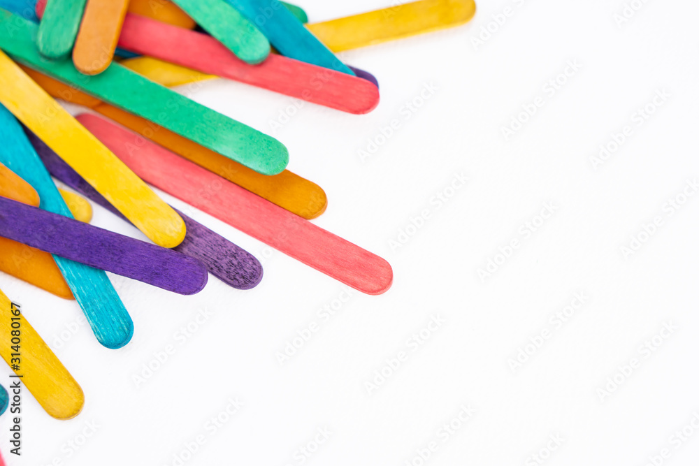 Colorful rainbow wooden popsicles on white paper background with copy space, abstract color sticks cover frame for children art craft works, kids back to school concept Colorful rainbow wooden popsicles on white paper background with copy space, abstract color sticks cover frame for children art craft works, kids back to school concept