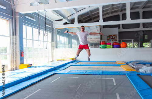 Fitness  fun  leisure and sport activity concept - Handsome happy man jumping on a trampoline indoors