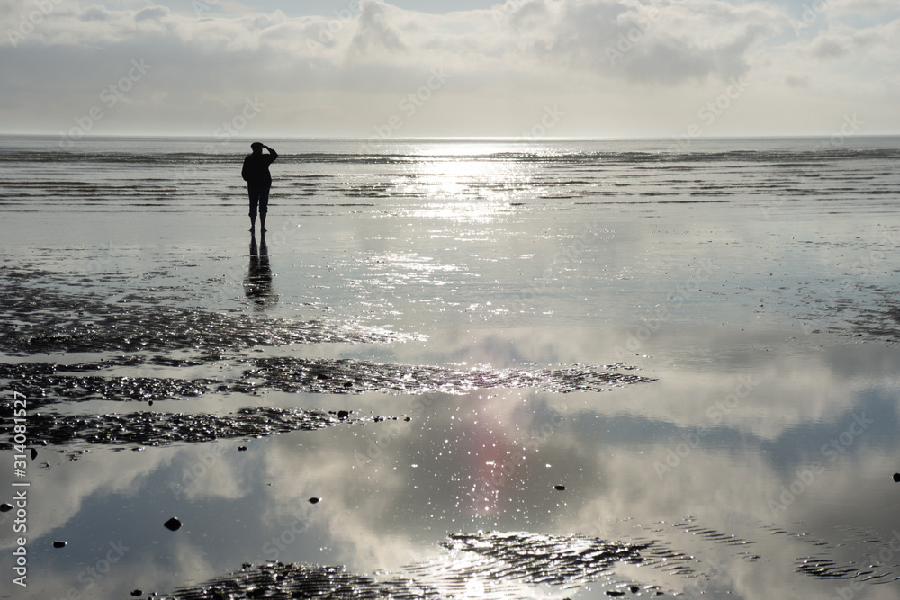 Man as a shilouette in the Wadden Sea of the North Sea in backlight and with reflection