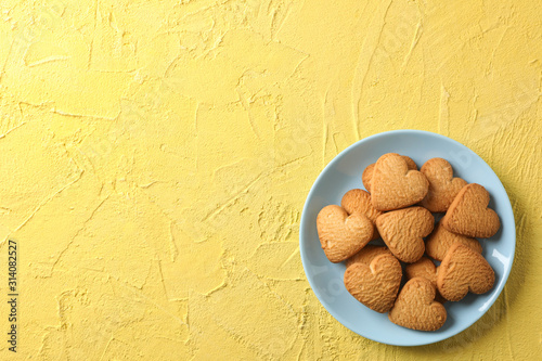 Plate with heart shaped cookies on yellow background, top view photo