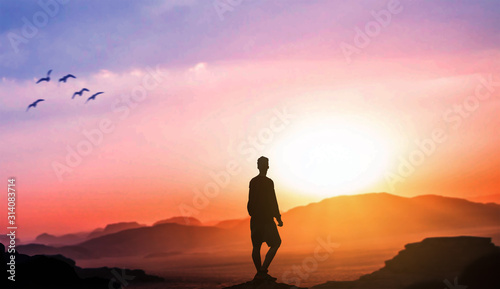 Man standing on top of mountain looks at the setting sun and the sunset horizon with a valley filled.