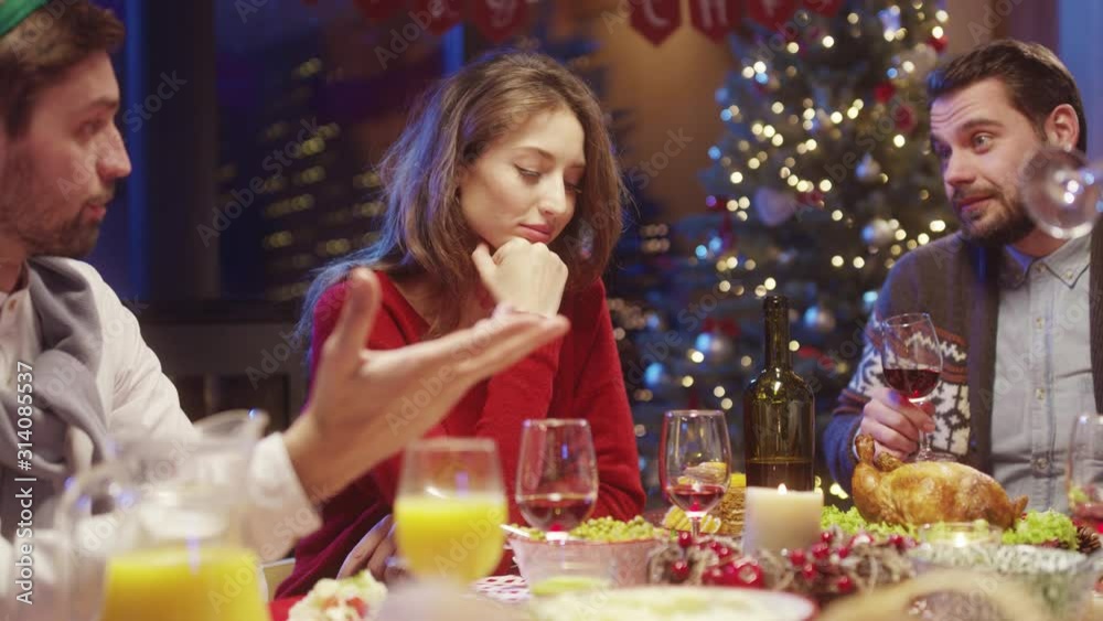 Sad Christmas story. Miserable pretty girl feeling alone at dinner party, sitting with friends at table together, suffering bad emotions. New Year celebration concept. Sad Christmas story. Miserable pretty girl feeling alone at dinner party, sitting with friends at table together, suffering bad emotions. New Year celebration concept.