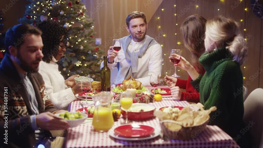 Handsome happy diverse men and women toasting with wine at table, gathering on Christmas holiday dinner, celebrating New Year's Eve together. Merry Christmas. Handsome happy diverse men and women toasting with wine at table, gathering on Christmas holiday dinner, celebrating New Year's Eve together. Merry Christmas.