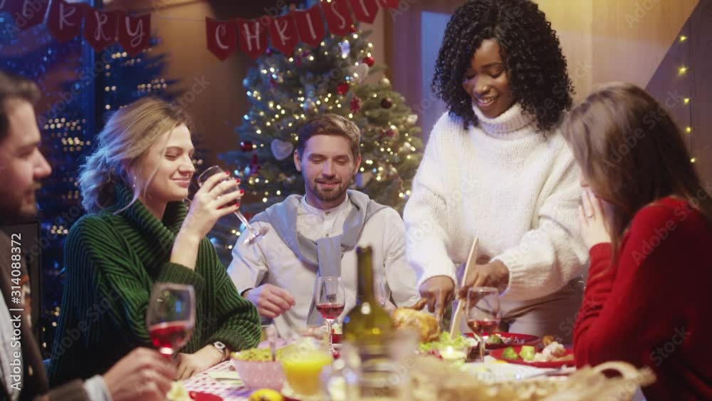 Beautiful black girl gathering friends at Christmas, carving hot turkey meal at dinner table, talking and socializing, enjoying reunion party at New Year's Eve. Beautiful black girl gathering friends at Christmas, carving hot turkey meal at dinner table, talking and socializing, enjoying reunion party at New Year's Eve.