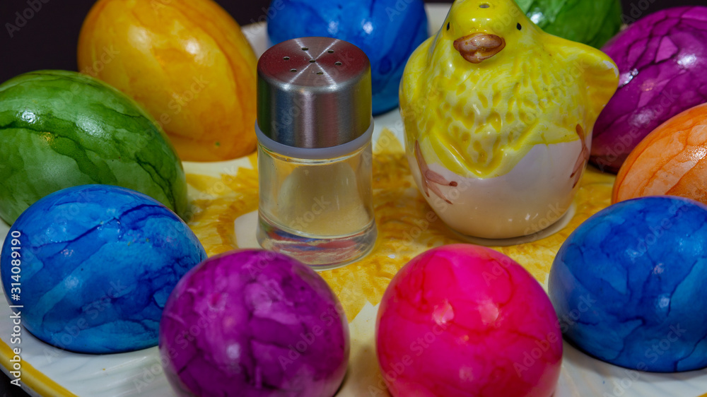 small salt shaker next to a clay chick and colorful Easter eggs