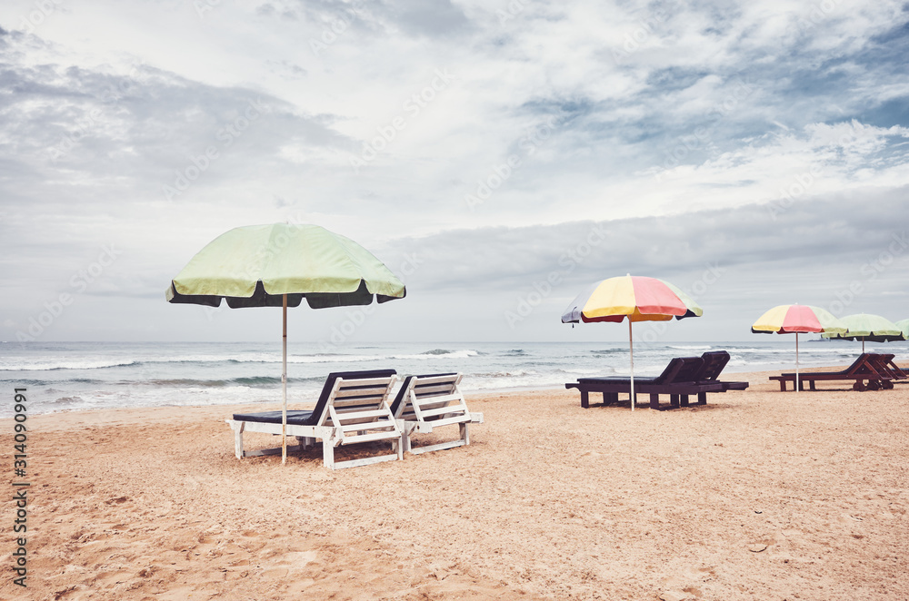 Sunbeds with umbrellas on an empty beach, color toning applied, Sri Lanka.