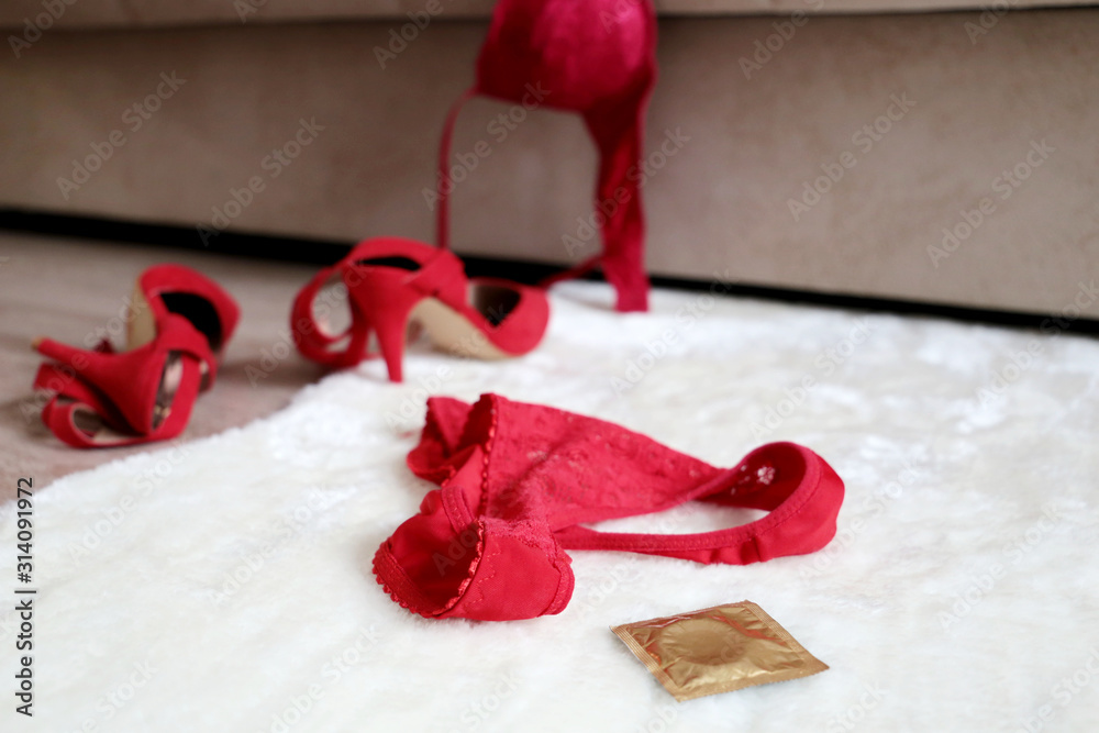 Red lace panties, bra, condom and shoes on high heels on the fur rug on a  floor near sofa. Quick sex concept, night of passion, female lingerie Stock  Photo