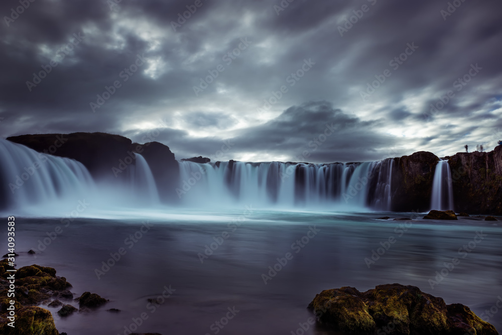 Fototapeta premium Cascades of waterfalls dropping down from the cliffs. Long exposure. Dramatic harsh landscape of cascades of waterfalls. Iceland. Waterfall Godafoss