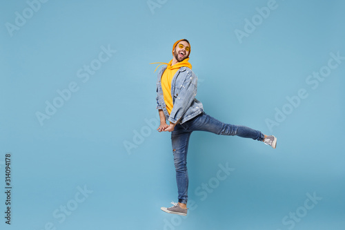 Funny young hipster guy in fashion jeans denim clothes posing isolated on pastel blue wall background studio portrait. People emotions lifestyle concept. Mock up copy space. Jumping spreading legs.