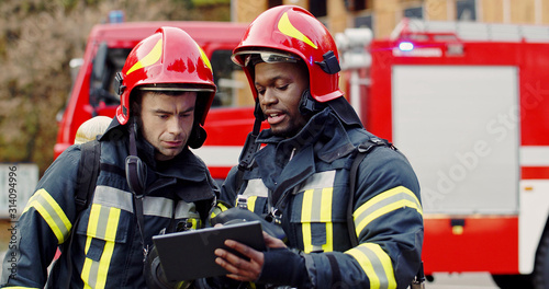 Portrait of two firefighters in fire fighting operation, fireman in protective clothing and helmet using tablet computer in action fighting.