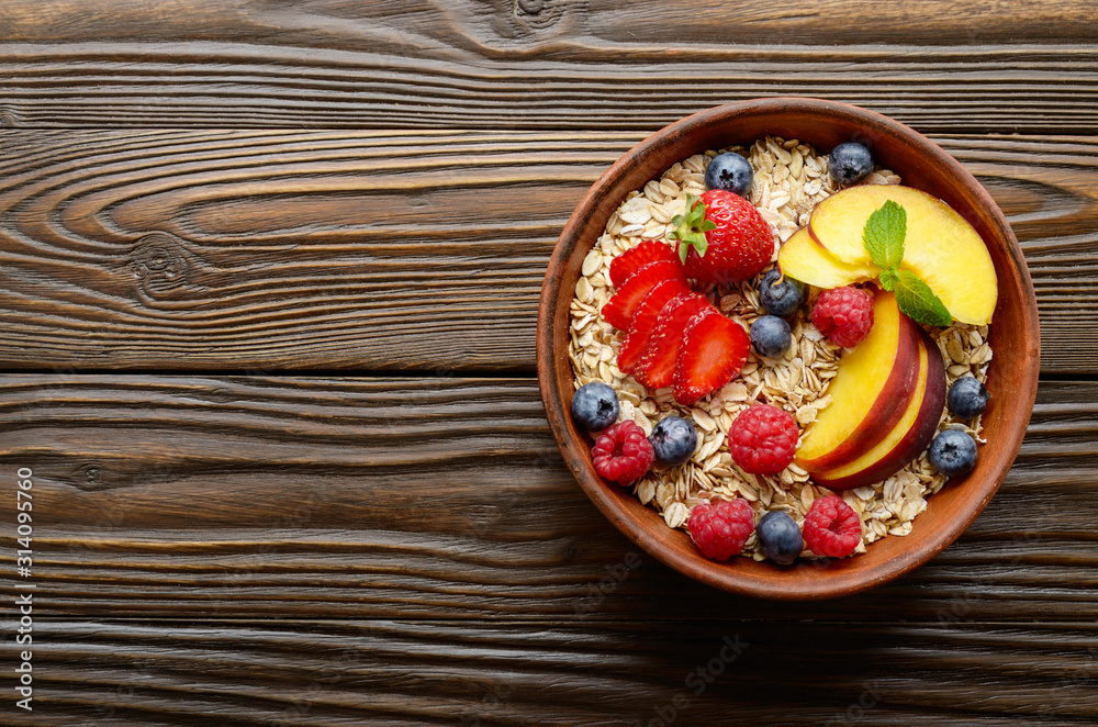 Flat lay of fruit healthy muesli with peaches strawberry almonds and blackberry in clay dish on wooden kitchen table Flat lay of fruit healthy muesli with peaches strawberry almonds and blackberry in clay dish on wooden kitchen table