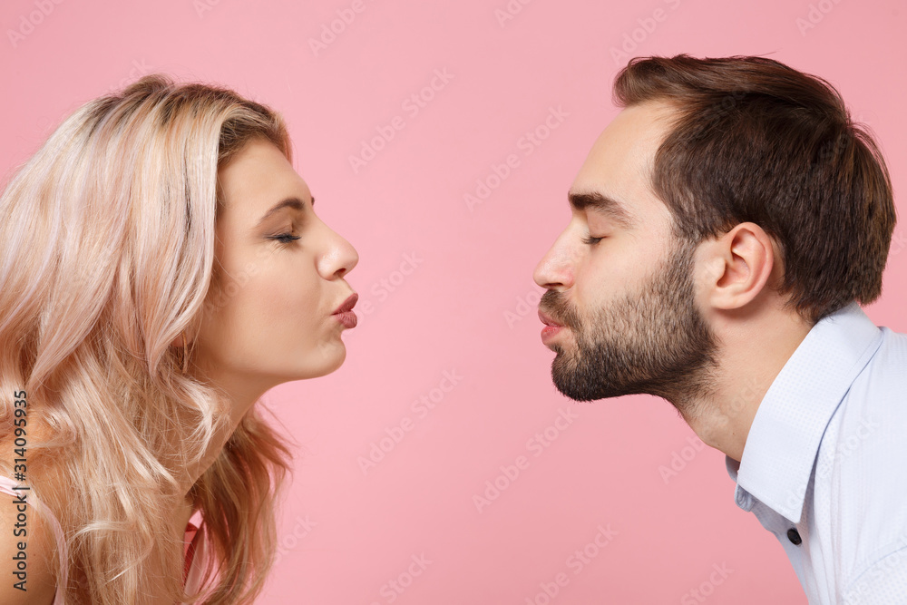 Side view of young couple two guy girl in party outfit celebrating posing isolated on pastel pink background in studio. People lifestyle Valentine's Day Women's Day birthday holiday concept. Kissing. Side view of young couple two guy girl in party outfit celebrating posing isolated on pastel pink background in studio. People lifestyle Valentine's Day Women's Day birthday holiday concept. Kissing.