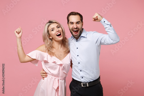 Joyful young couple two guy girl in party outfit celebrate posing isolated on pastel pink background. People lifestyle Valentine's Day Women's Day birthday holiday concept. Clenching fist like winner.