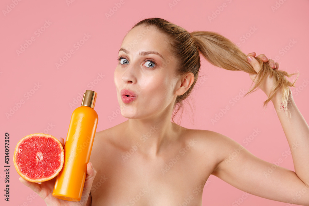 Close up half naked woman 20s perfect skin nude makeup blue eyes hold grapefruit bottle of shampoo isolated on pastel pink background studio portrait Skin care healthcare cosmetic procedures concept. Close up half naked woman 20s perfect skin nude makeup blue eyes hold grapefruit bottle of shampoo isolated on pastel pink background studio portrait Skin care healthcare cosmetic procedures concept.