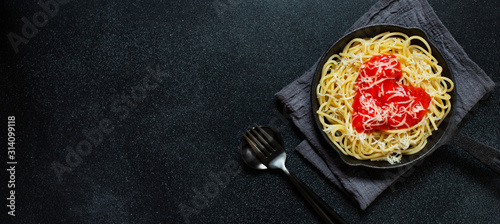 Spaghetti pasta with heart shaped tomato sauce, served in a pan. Dinner for Valentine's Day. Food with love. Top view, flat lay, black background