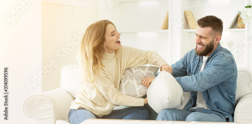 Playful millennial couple fighting by pillows, having fun