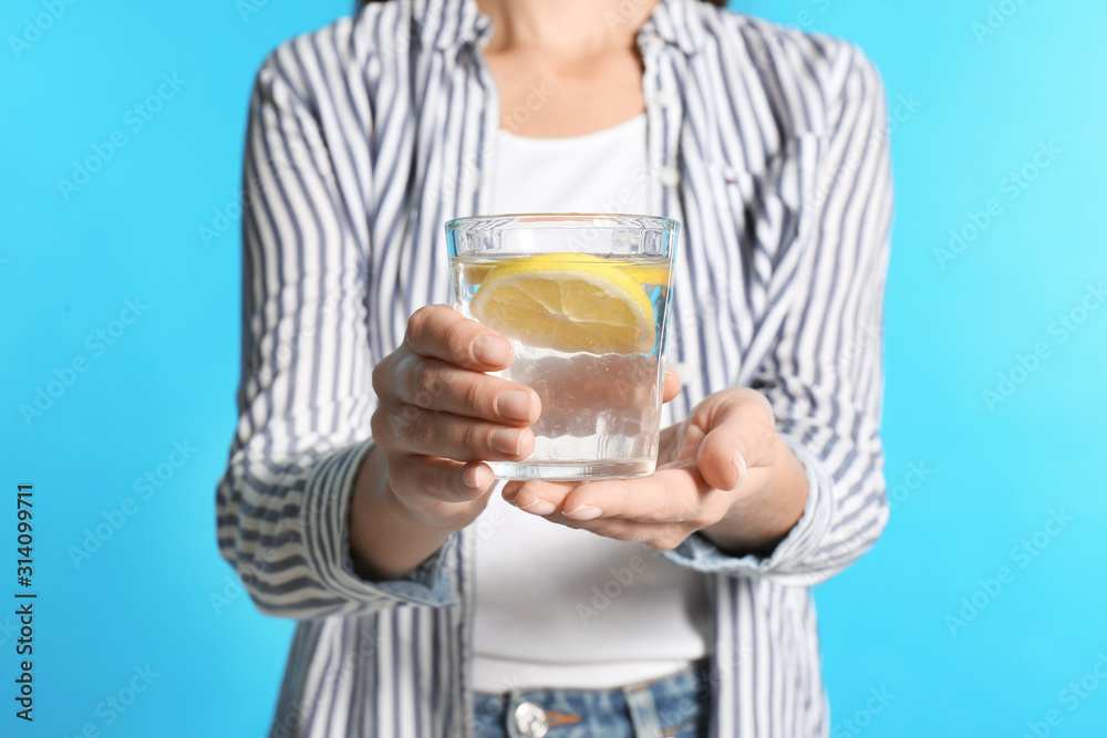 Young woman with glass of lemon water on light blue background, closeup Young woman with glass of lemon water on light blue background, closeup