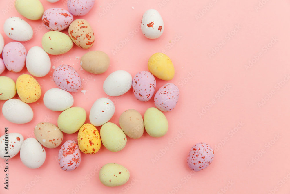 Happy Easter concept. Easter candy chocolate eggs and jellybean sweets isolated on trendy pastel pink background. Simple minimalism flat lay top view copy space
