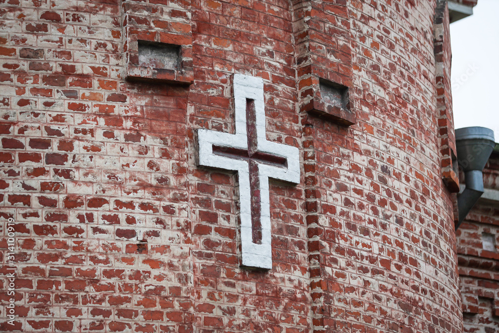 Old brick church wall with white cross sign on the side of building.