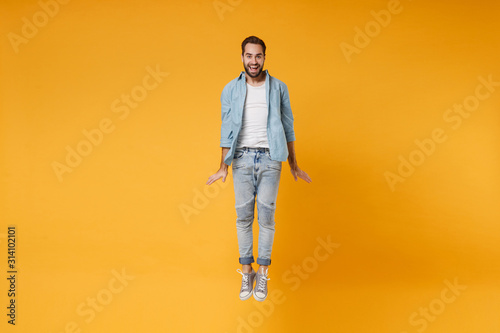 Cheerful young bearded man in casual blue shirt posing isolated on yellow orange wall background, studio portrait. People sincere emotions lifestyle concept. Mock up copy space. Jumping, having fun.